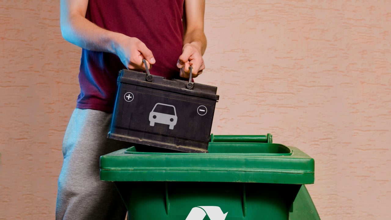 Man throwing old empty car battery in garbage disposal with recycling symbol