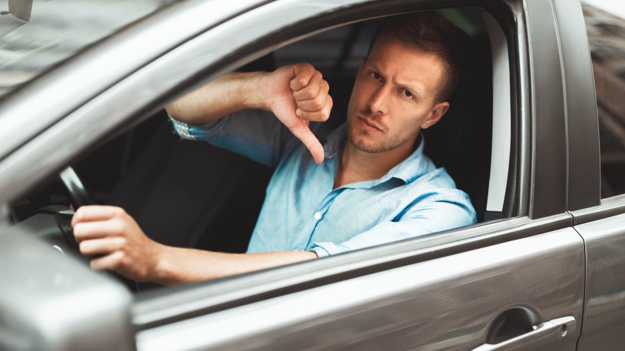 young handsome man sitting in his car showing dislike sign