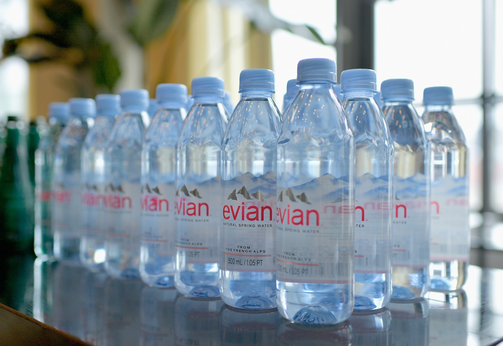 Rows of Evian bottled water on a table, with blurred plant in the background. Labels say natural spring water.