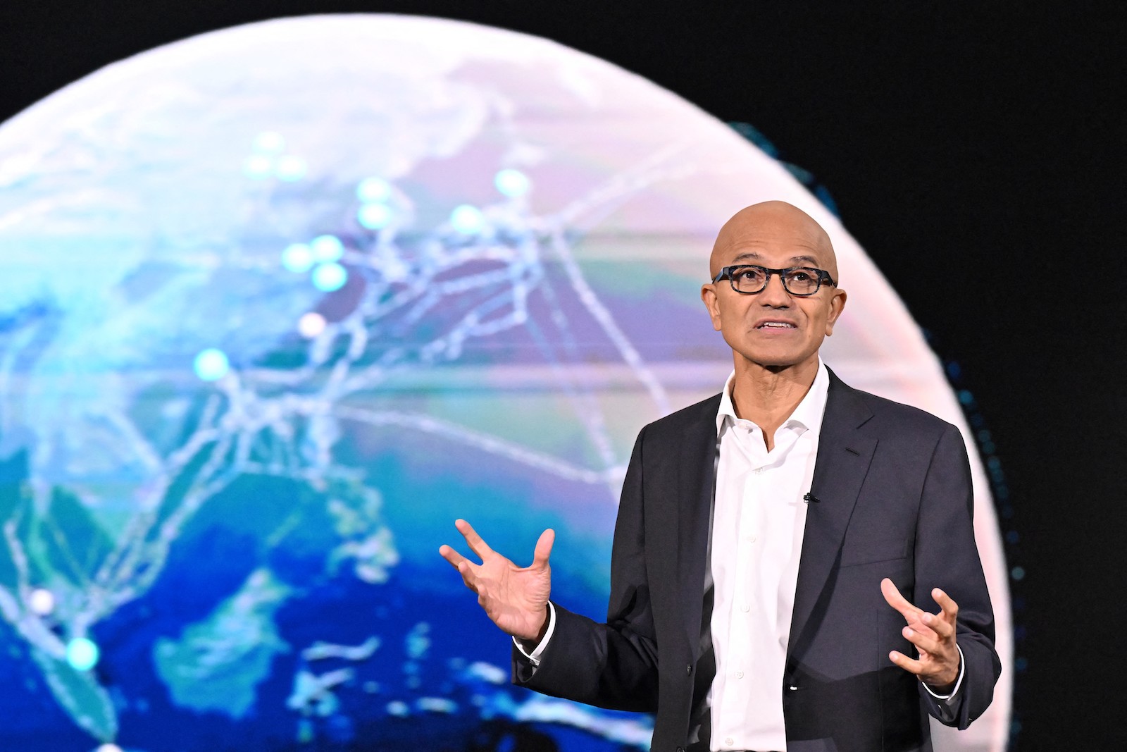 A man in a suit with glasses talks in front of an Earth icon