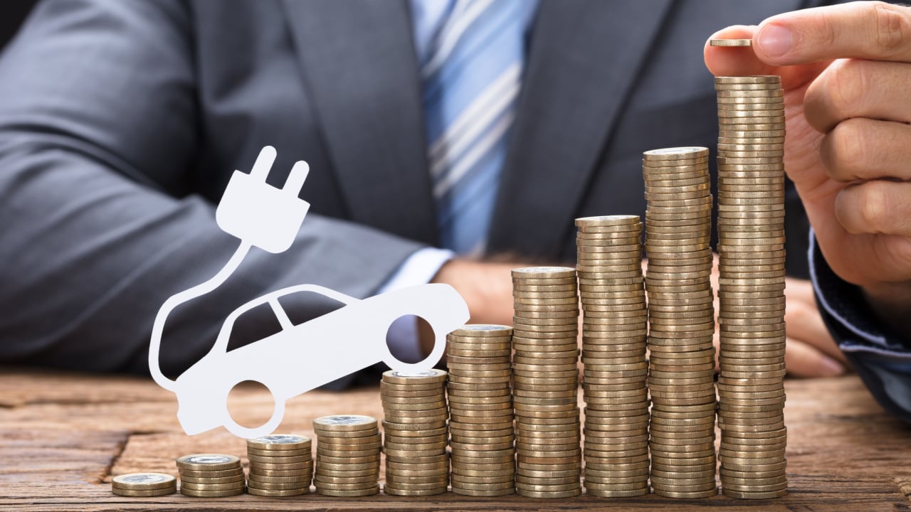 Midsection of businessman stacking coins with electric car at wooden table