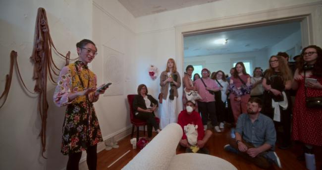 group of people gathered around a room with an artist speaking