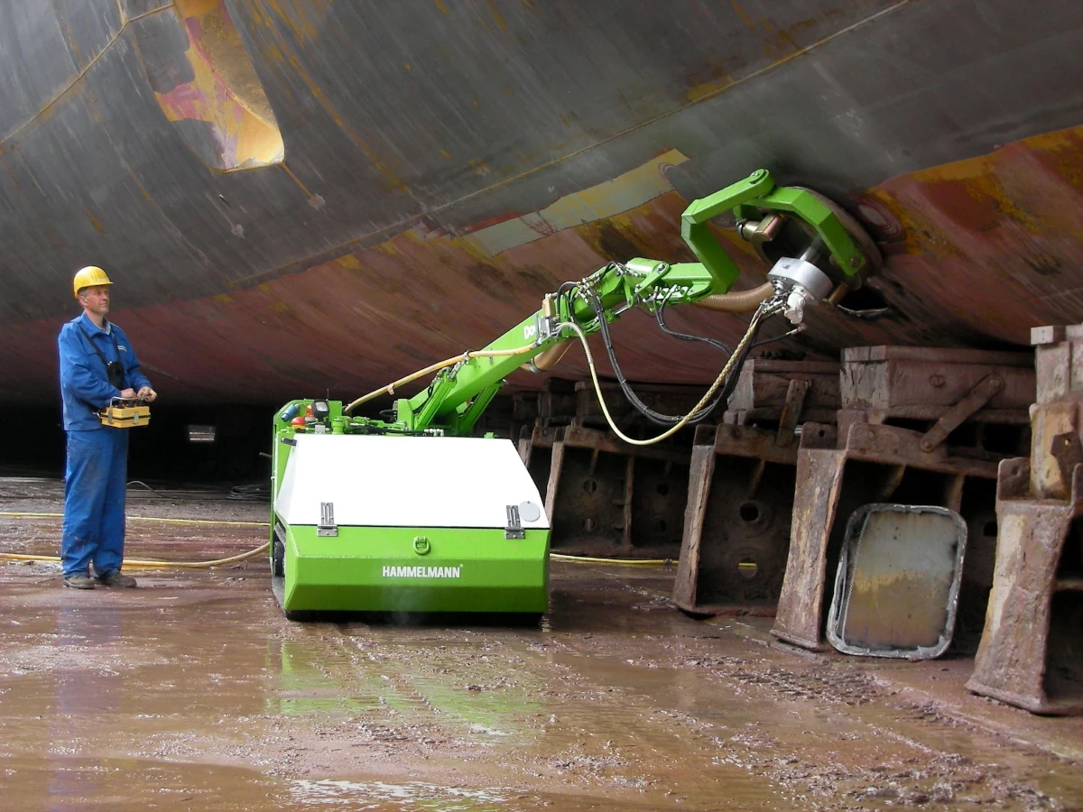 Worker and green-coloured machine underneath the hull of a ship, which is mounted in drydock